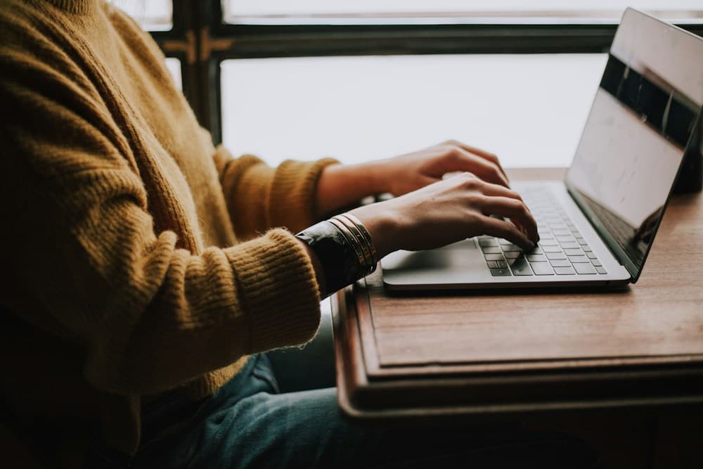 Close-up of hands typing on a laptop by a window